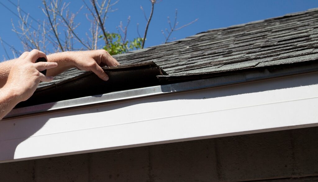 A person inspecting shingles near the gutter.