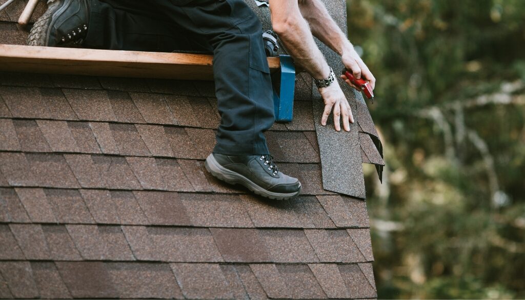 Roofing contractor cleaning up shingles on the edge of the roof line.