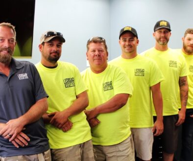 Ledegar Roofing employees wearing matching t-shirts smile as a group.