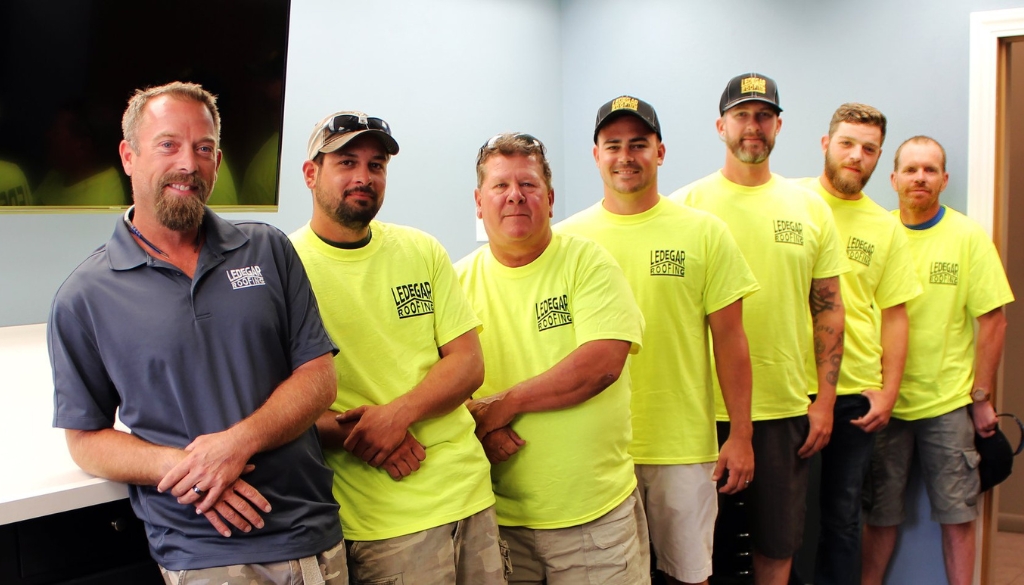 Ledegar Roofing employees wearing matching t-shirts smile as a group.