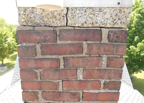 A brick residential chimney in need of repair due to cracking.