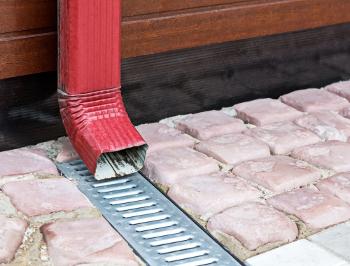 The bottom of a residential home downspout on to an outdoor floor drain.