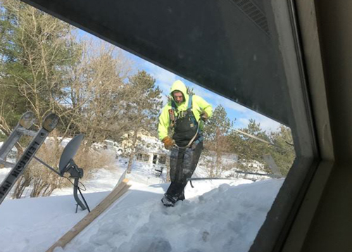 A Ledegar Roofing employee on top of a residential roof, preparing to remove heavy snow.