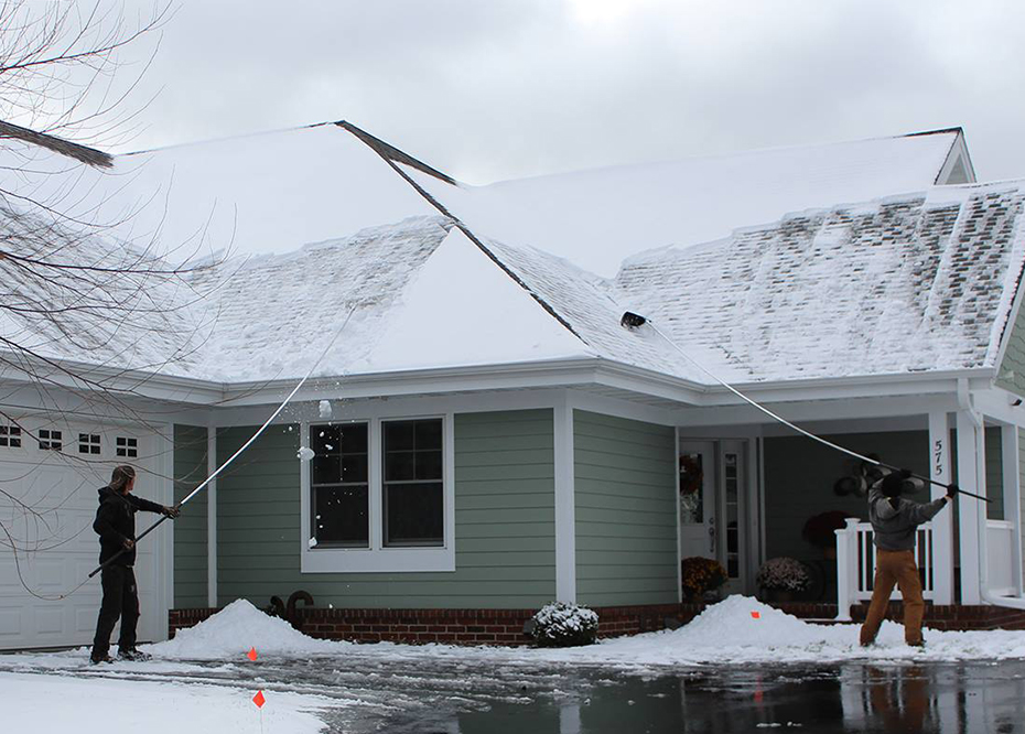 Two Ledegar Roofing employees removing snow off a residential roof in winter.