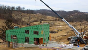 A sheet metal worker operates a forklift crane as Ledegar Roofing employees work to add a roof to a commercial building.