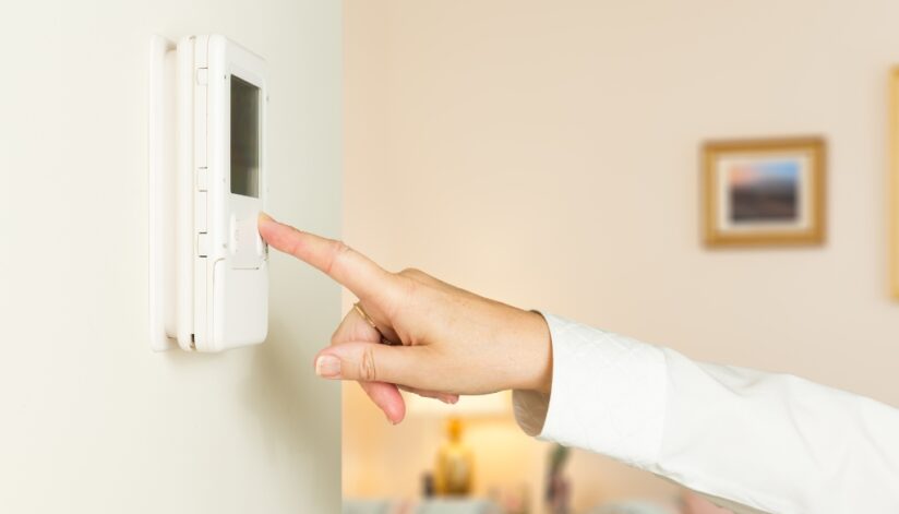 A person changing the temperature on a thermostat to reduce home's energy use.