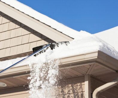 A residential roof with inches of snow on it, and a roof rake removing some of it.