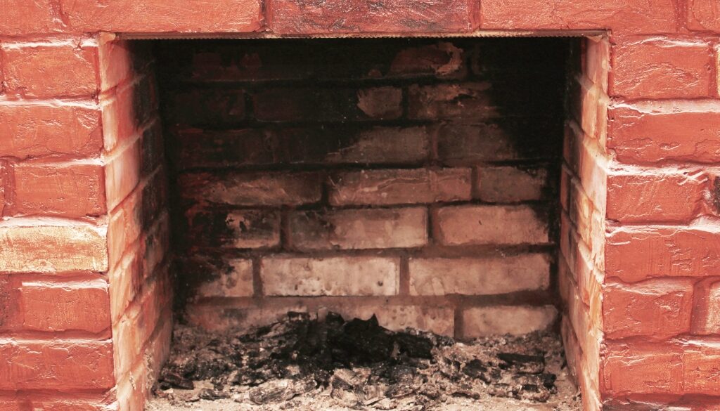 A dirty, red brick fireplace and chimney in need of a professional cleaning.