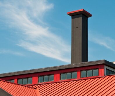 A commercial building with a red roof and black commercial chimney with a blue sky behind it.