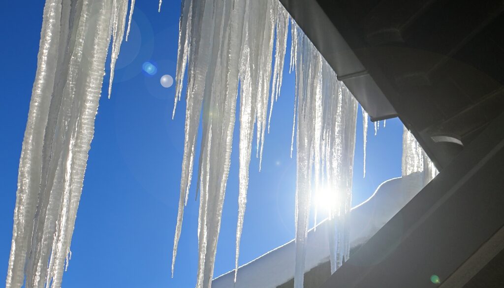 "Icicles hanging from a roofline against a bright blue sky.