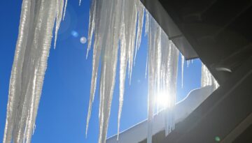 "Icicles hanging from a roofline against a bright blue sky.