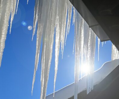 "Icicles hanging from a roofline against a bright blue sky.