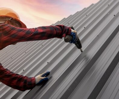 Worker in safety gear installing a sleek metal roof under a vibrant sunset sky.