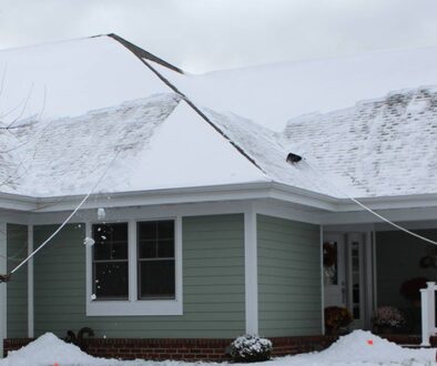 Two people using roof rakes to safely remove snow from a residential roof during winter