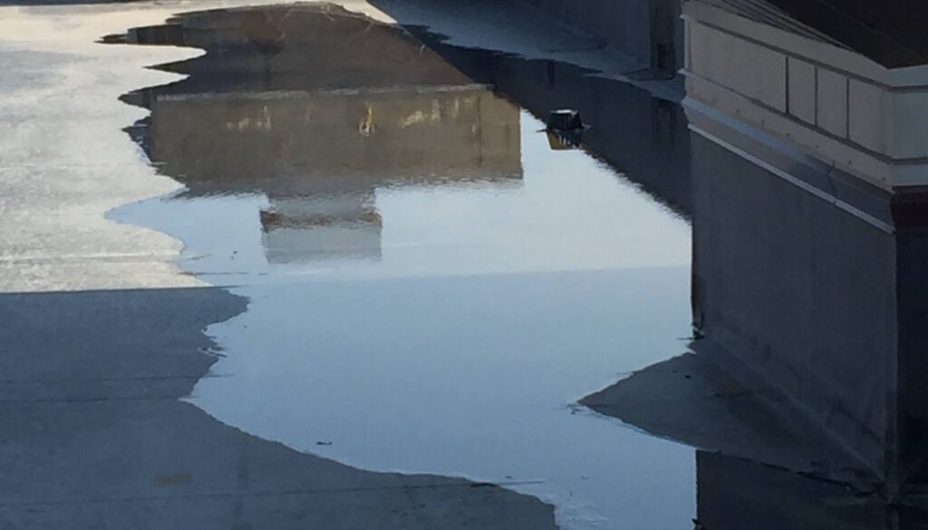 Standing water on a flat commercial roof, indicating potential spring thaw roof damage and drainage issues.