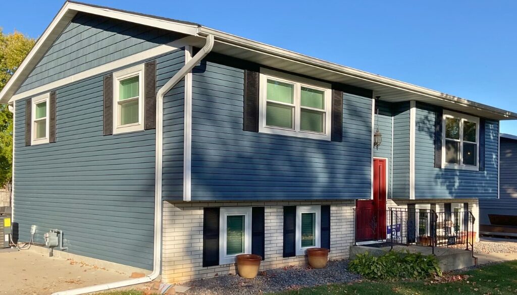 A renovated split-level home with new seamless gutters installed by Ledegar Roofing, featuring blue siding, white trim, and a red front door in West Salem, WI.