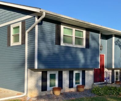 A renovated split-level home with new seamless gutters installed by Ledegar Roofing, featuring blue siding, white trim, and a red front door in West Salem, WI.