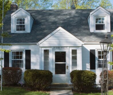 A well-maintained white home with a dark gray shingle roof, black shutters, and a manicured front yard.