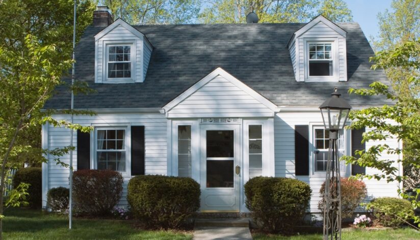 A well-maintained white home with a dark gray shingle roof, black shutters, and a manicured front yard.