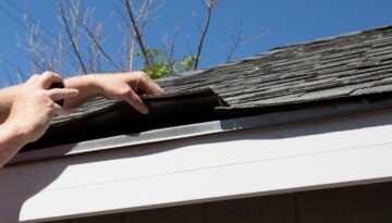 A contractor lifts damaged asphalt shingles during a free roof inspection to check for hidden issues.