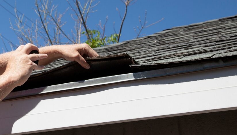 A contractor lifts damaged asphalt shingles during a free roof inspection to check for hidden issues.
