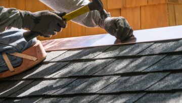 A roofing contractor installs metal flashing over asphalt shingles on a residential roof.