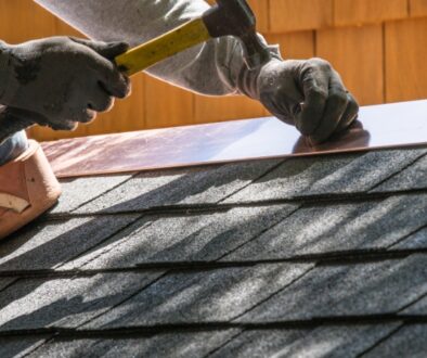 A roofing contractor installs metal flashing over asphalt shingles on a residential roof.
