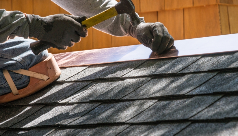 A roofing contractor installs metal flashing over asphalt shingles on a residential roof.