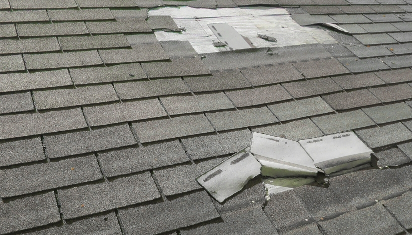 Damaged asphalt shingle roof with torn and missing shingles exposing underlayment and patched areas.