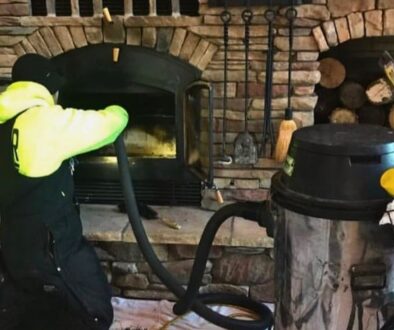 A Ledegar Roofing professional cleaning out a home fireplace and chimney.