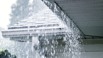 Heavy rain falling on a home with overflowing gutters.