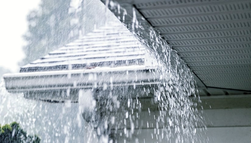 Heavy rain falling on a home with overflowing gutters.